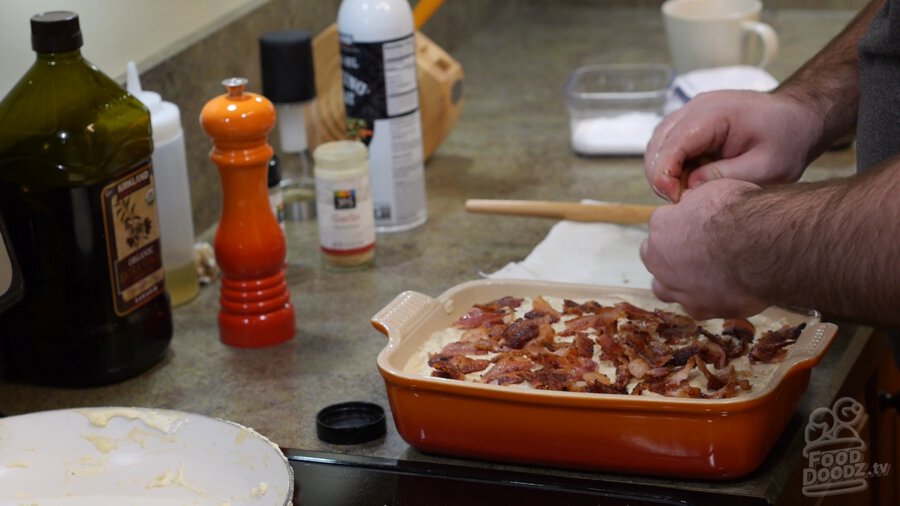 tearing and crumbling up bacon that is being spread across top of casserole