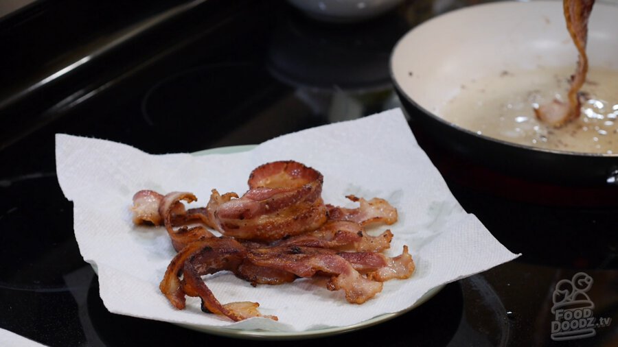 Cooked bacon cooling on a paper towel lined plate