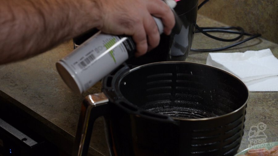 Spraying the inside of the air fryer basket with oil