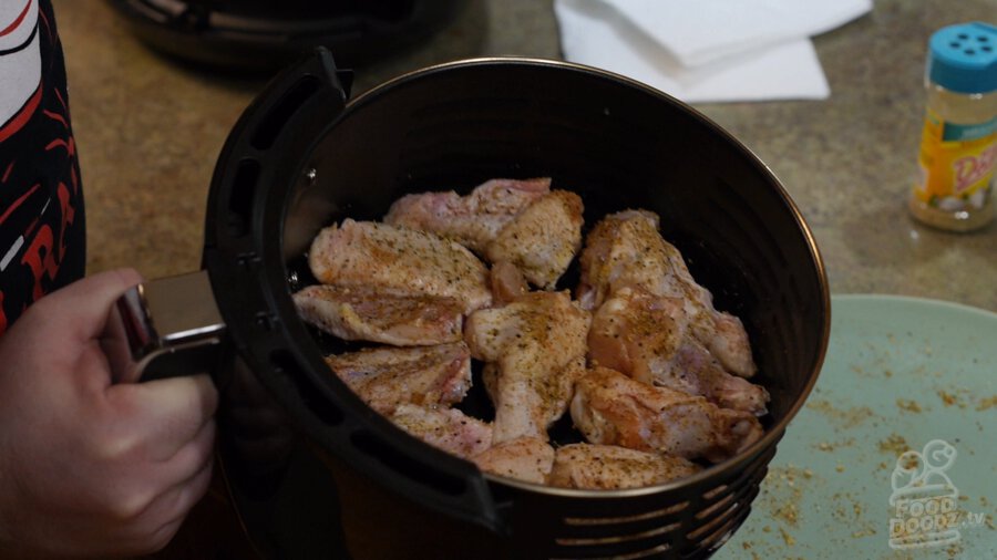 The air fryer tray evenly loaded with raw wings