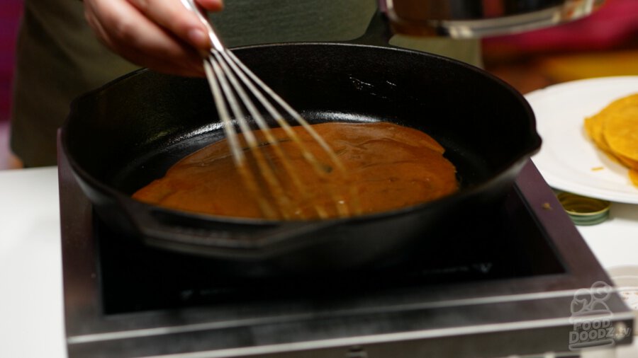 Spreading enchilada sauce over the bottom of a cast iron pan