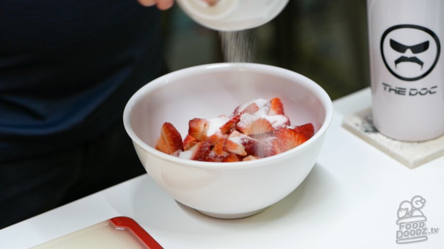 Adding 1/2 cup of sugar to sliced strawberries