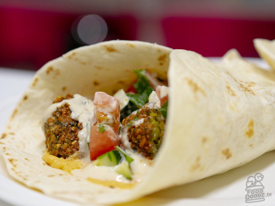 A mouth watering wrap of freshly fried falafel with hummus, cucumber tomato salad, and tahini sauce