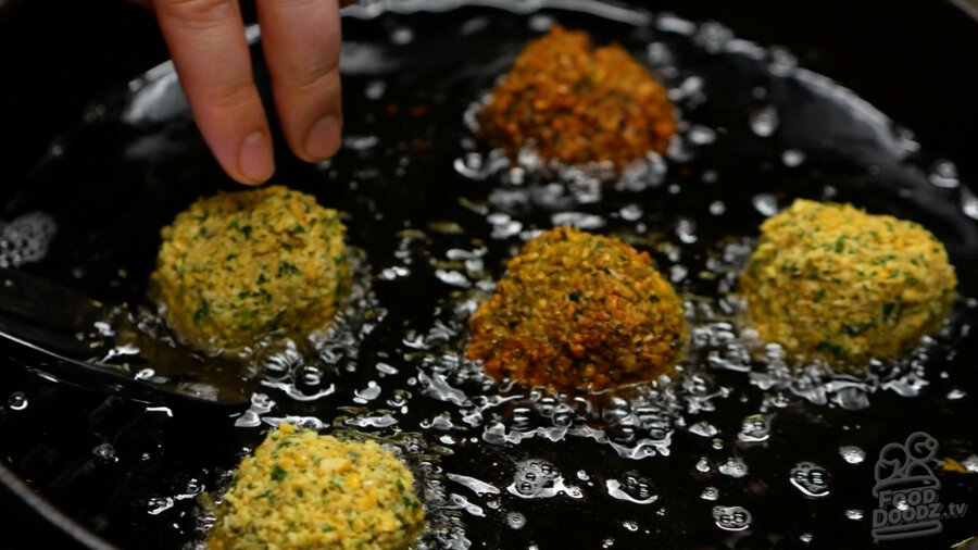 Falafels frying in the oil and various stages of doneness