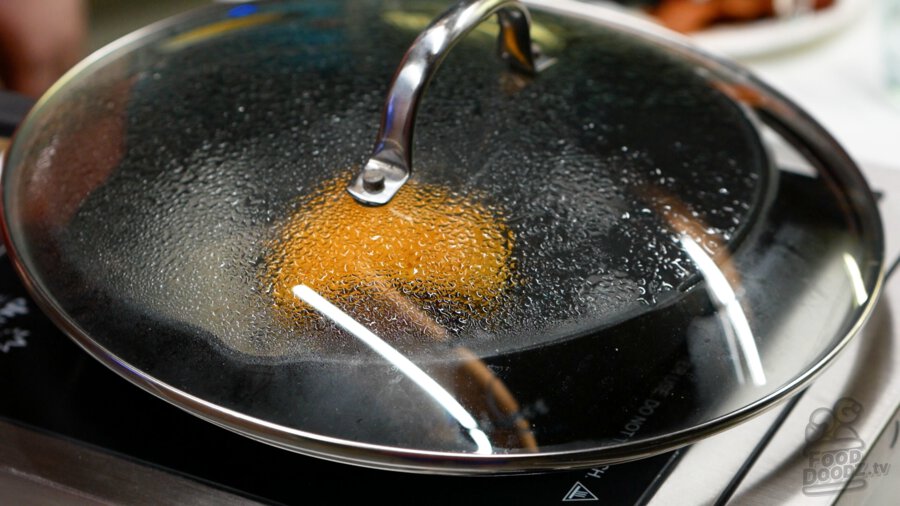 Covering the pan with a lid after adding a splash of water to it