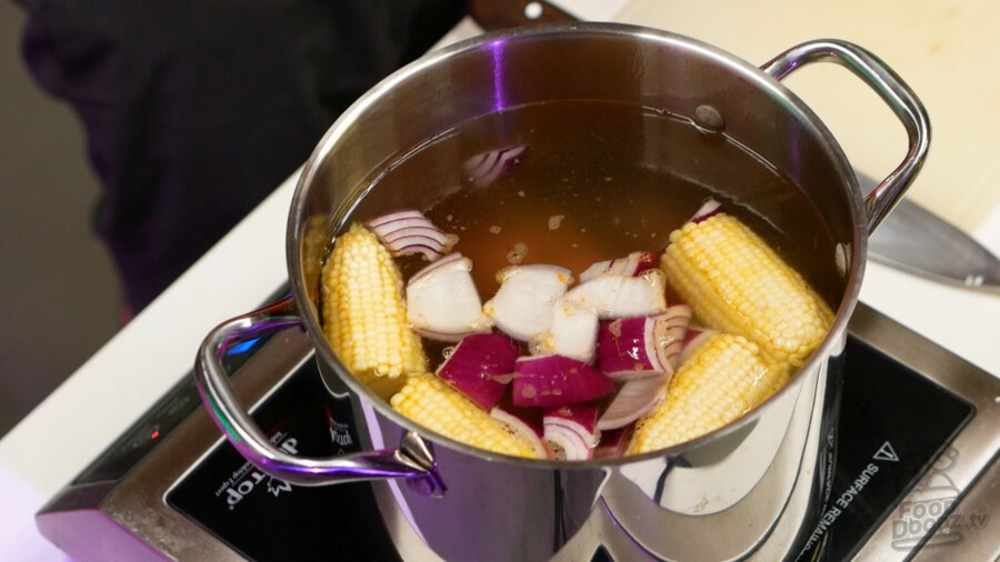 Adding corn, sausage, and onion to pot