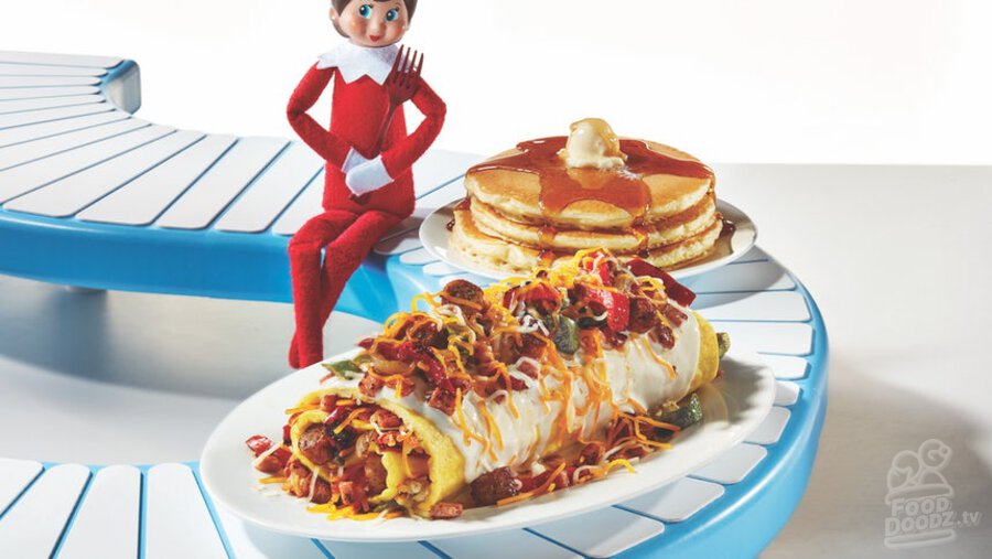 IHOP Holiday Ham & Sausage Omelette filled with ham, sausage, peppers, and onions. Then topped with more ham and sausage, cheddar cheese, and a white cheddar cheese sauce. Served with 3 pancakes