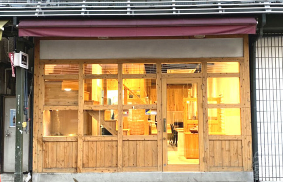 Front of VEGAN STORE in Asakusa Tokyo Japan. A wooden store front with large windows lets you see into a warmly lit dining area and a staircase leading up.