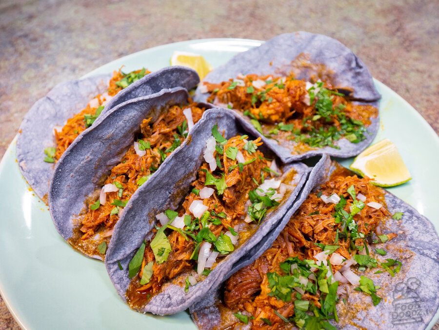 A plate of carnita tacos on corn tortillas with plenty of lime, cilantro and onion.