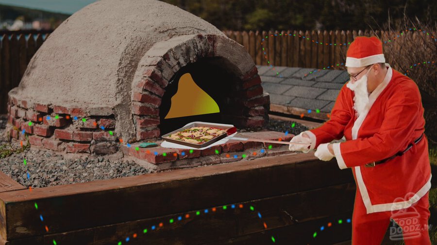 Austin dressed as Santa using peel to put pizza in brick fired pizza oven