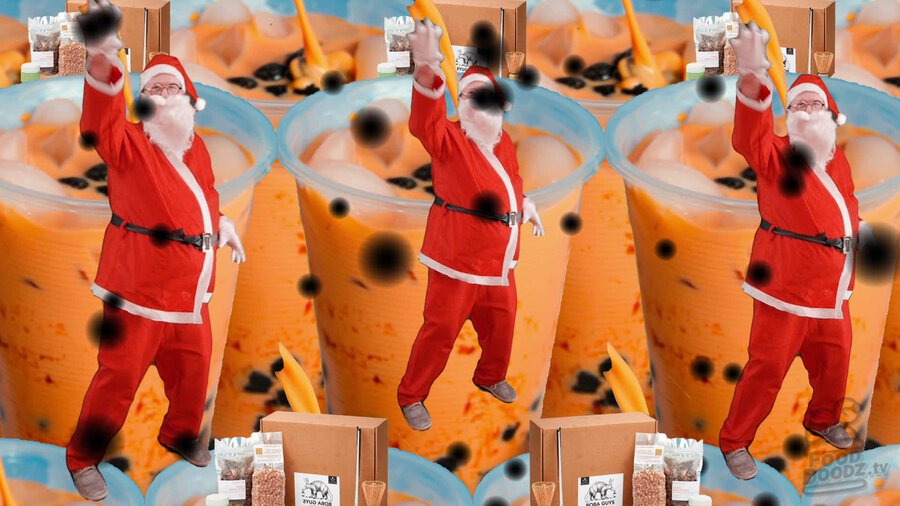 Austin dressed as Santa trying to grab and pop bubbles floating in front of giant boba tea cups behind him