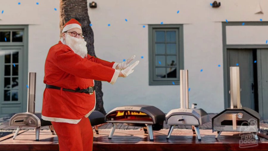 Austin dressed as Santa trying to stay warm in front of row of Ooni pizza ovens